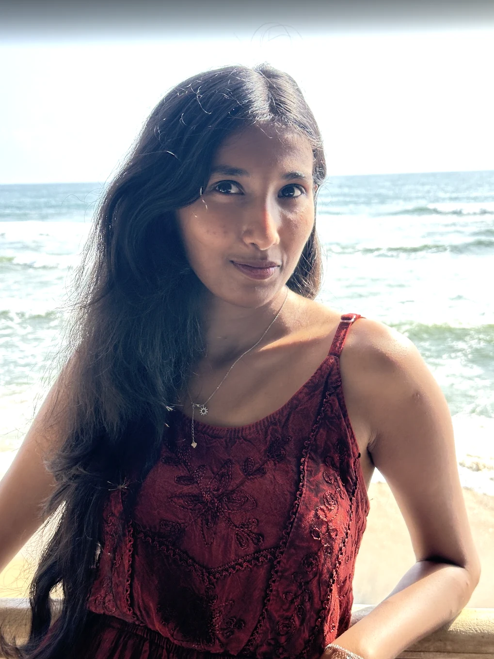 Harshitha by the sea in a red patterned outfit.